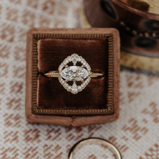 Diamond halo ring in a brown velvet box on a textured fabric surface