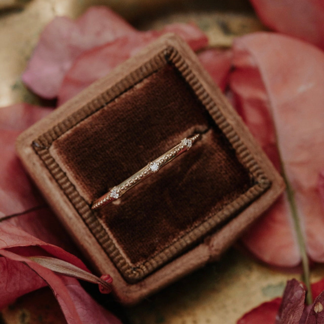Gold band  in a brown velvet box with pink leaves and a gold surface
