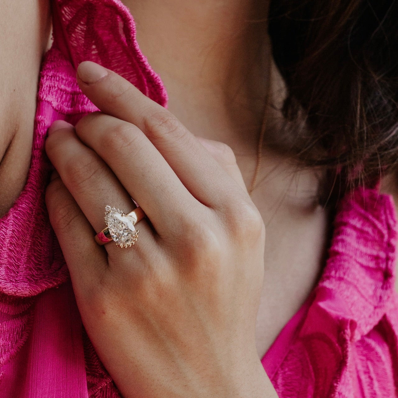 Close-up of a hand wearing a ring with pear diamond with a pink garment in the background