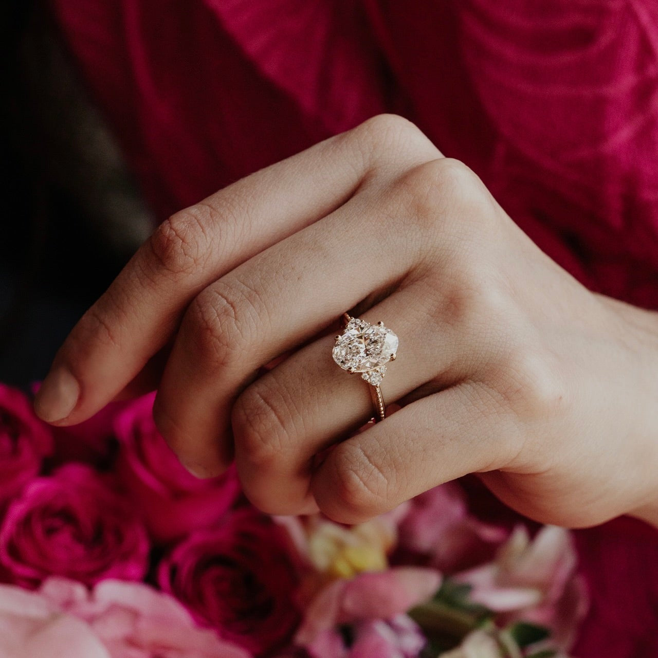 Hand wearing a oval diamond ring with pink roses in the background