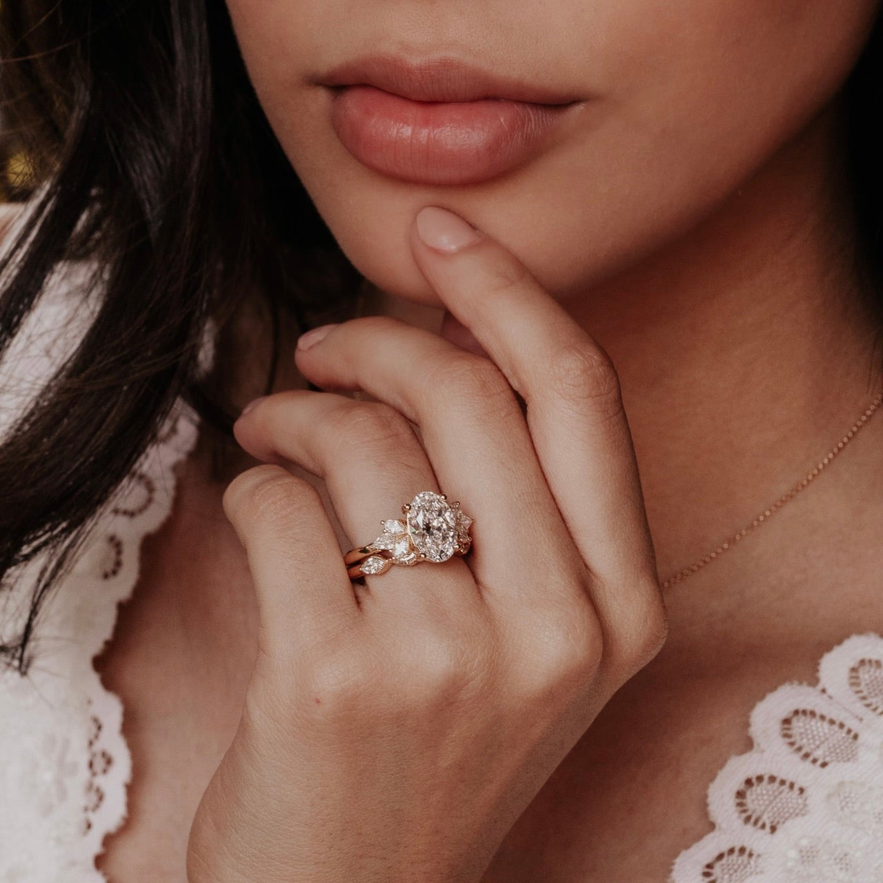 Close-up of a woman's hand with a oval diamond ring, wearing a white lace top.