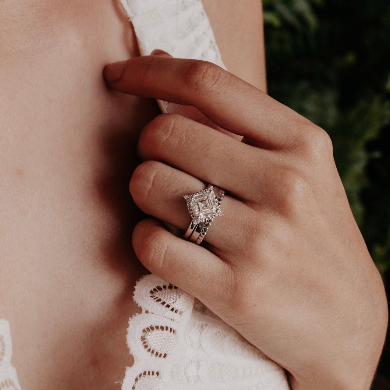 Close-up of a hand wearing an engagement ring with a blurred natural background