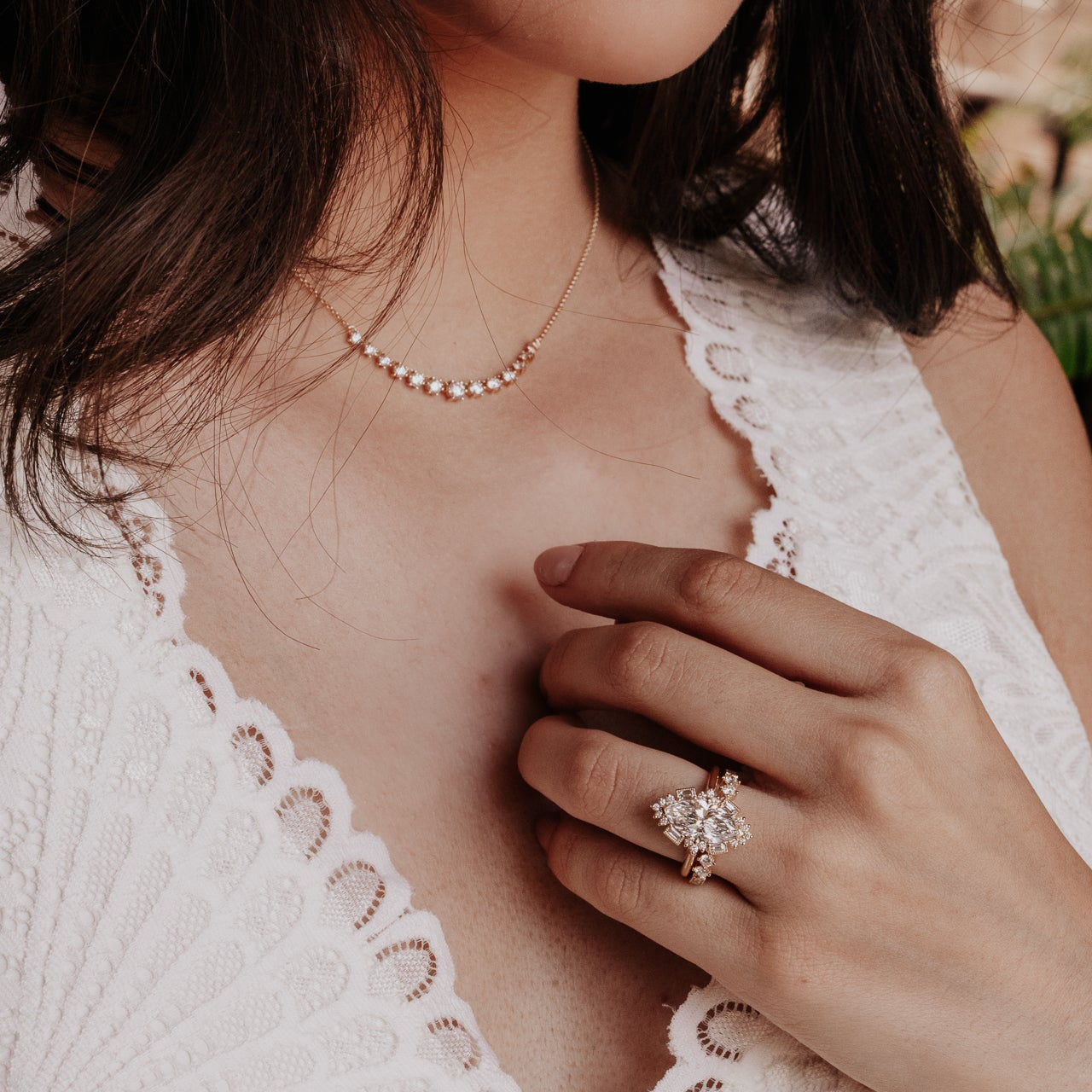 Close-up of a woman wearing a diamond necklace and a diamond ring on her finger.