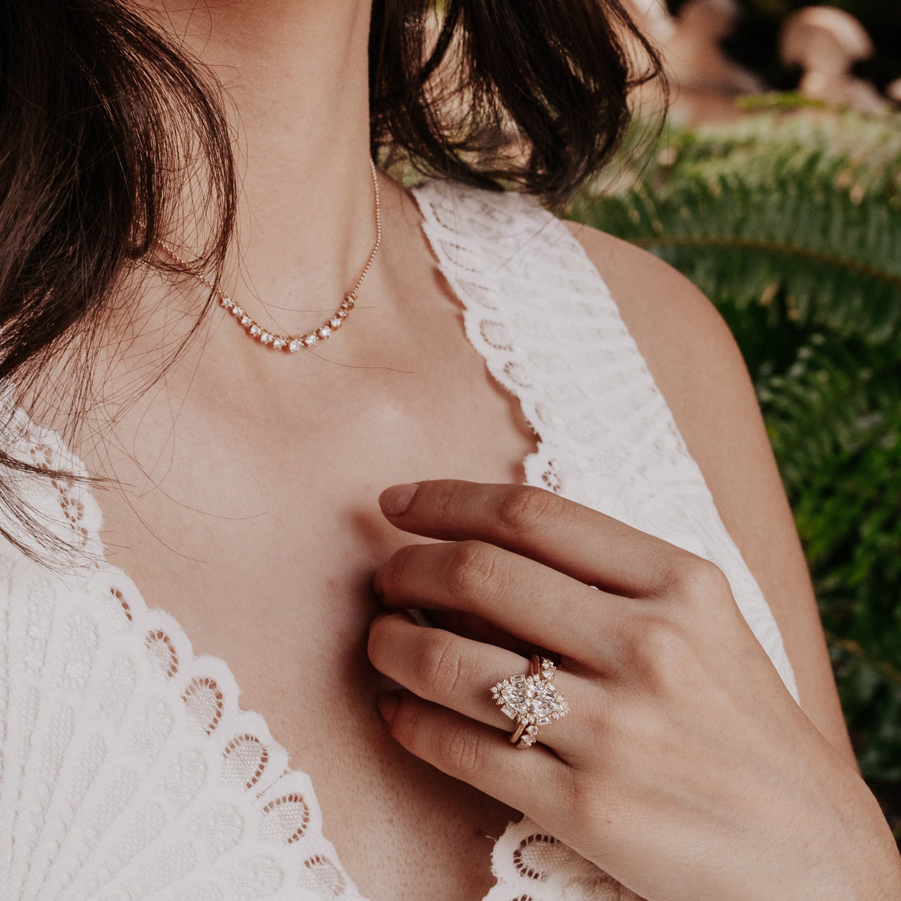 Close-up of a person wearing a necklace and diamond ring with a blurred natural background