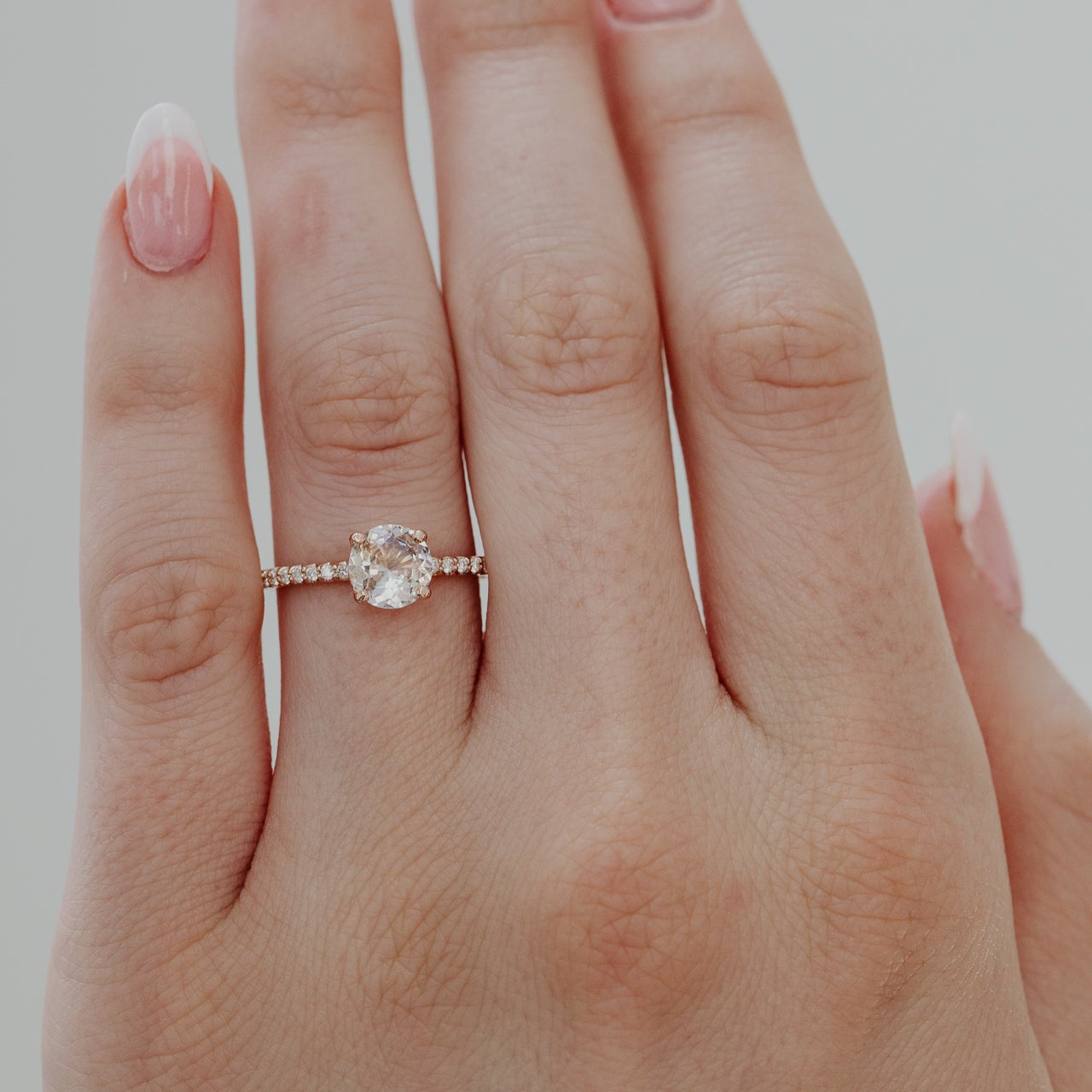 Close-up of a hand wearing a rose gold ring with a light pink Sri Lanka Sapphire and a pave diamond band on a plain background