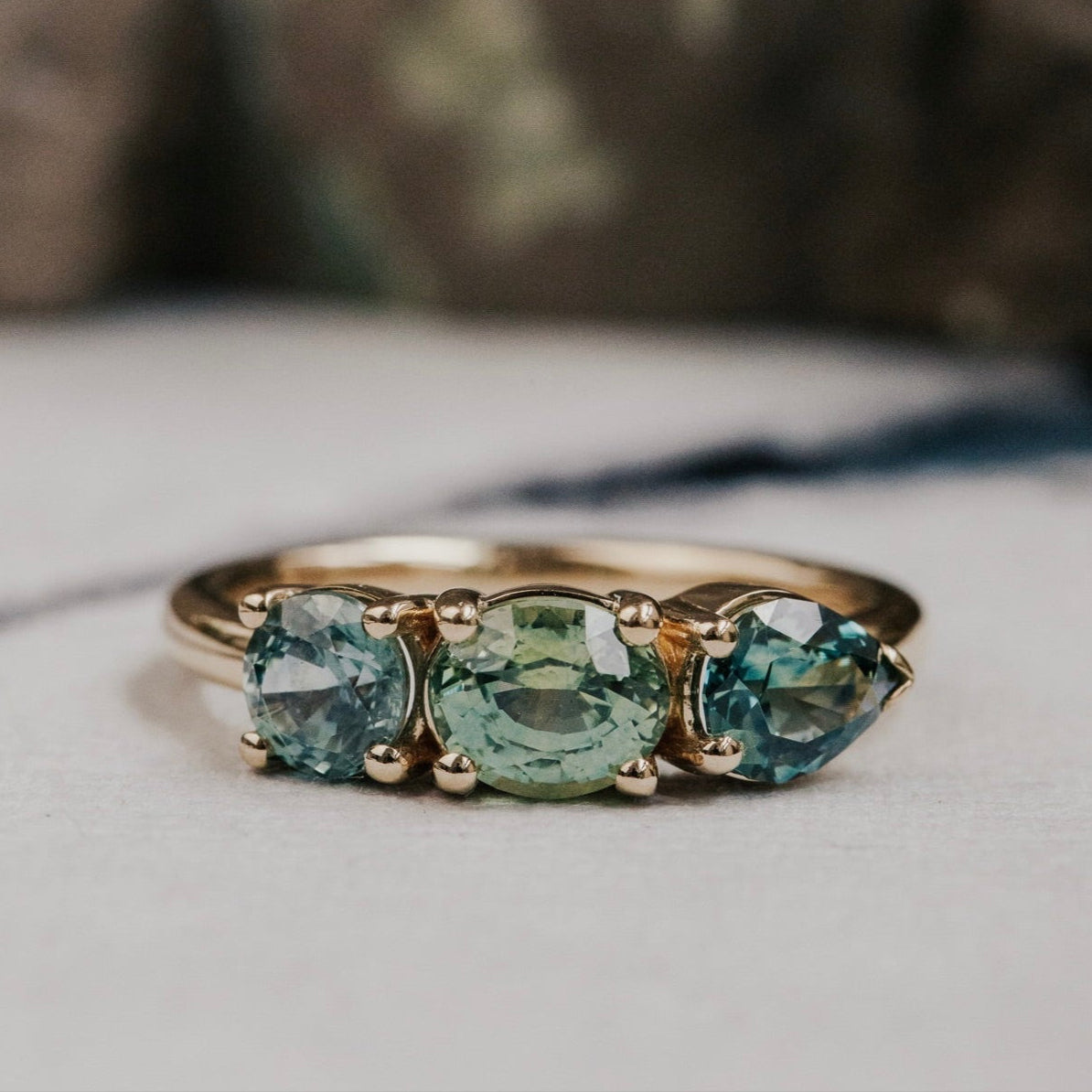 Gold ring with three green sapphires on a neutral background
