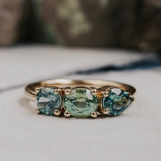 Gold ring with three green sapphires on a neutral background