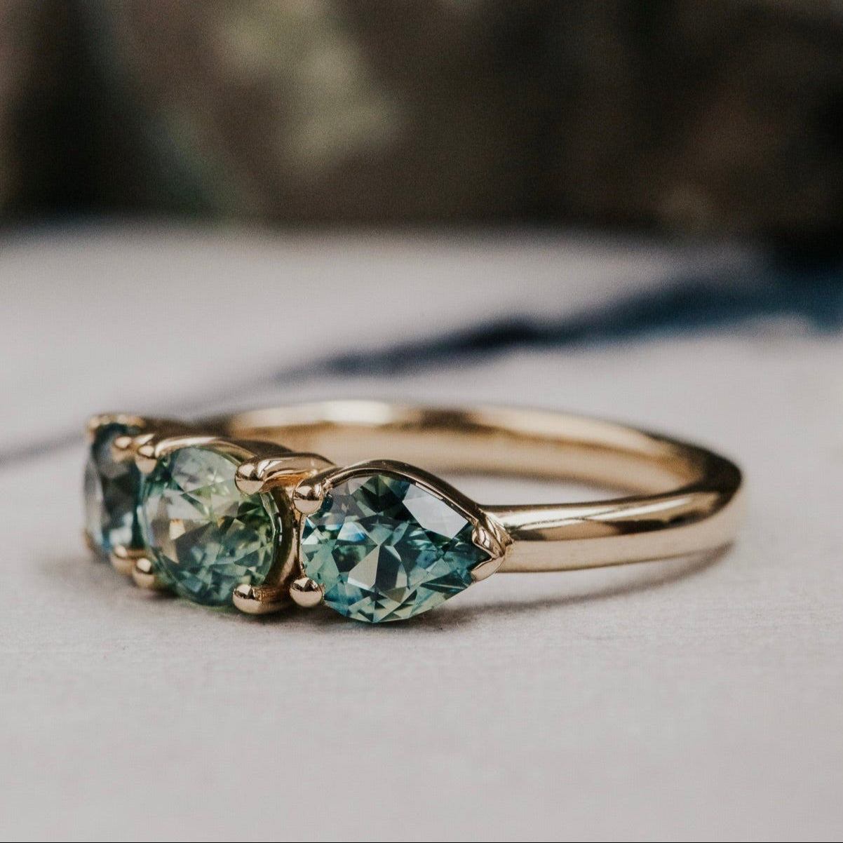 Gold ring with three green Montana sapphires on a neutral background