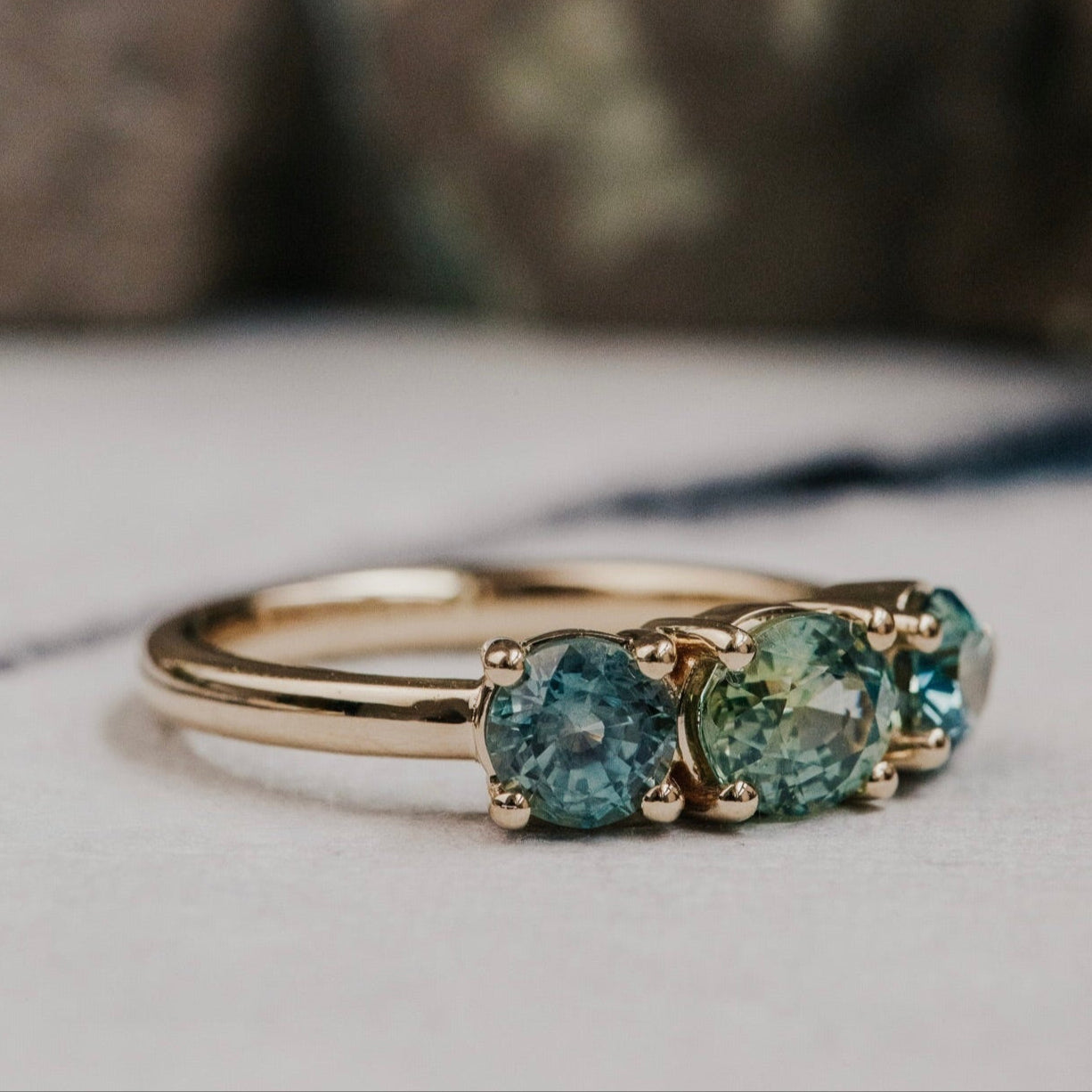 Gold ring with three green Montana Sapphires on a textured surface