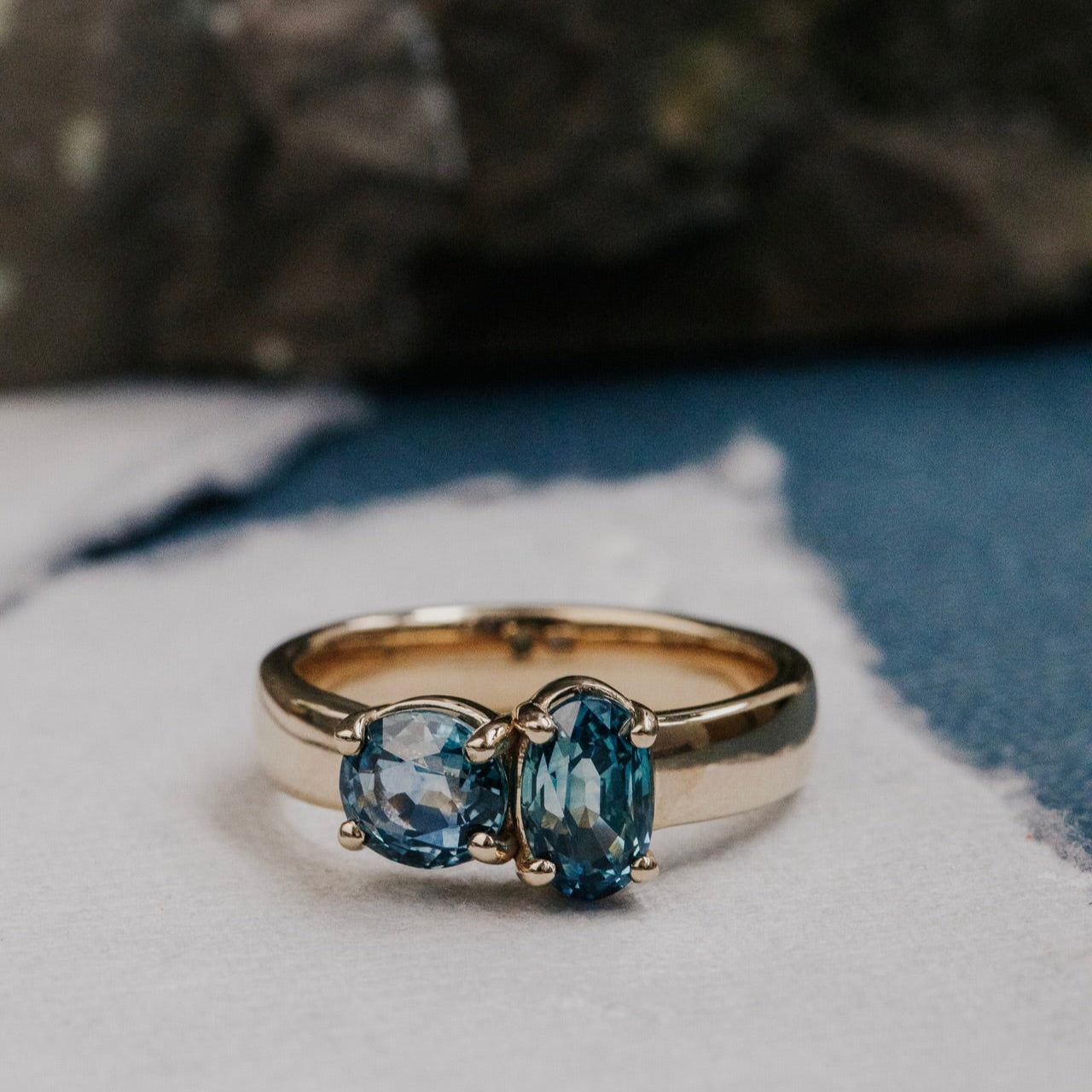 Gold ring with blue Montana sapphire gemstones on a textured surface