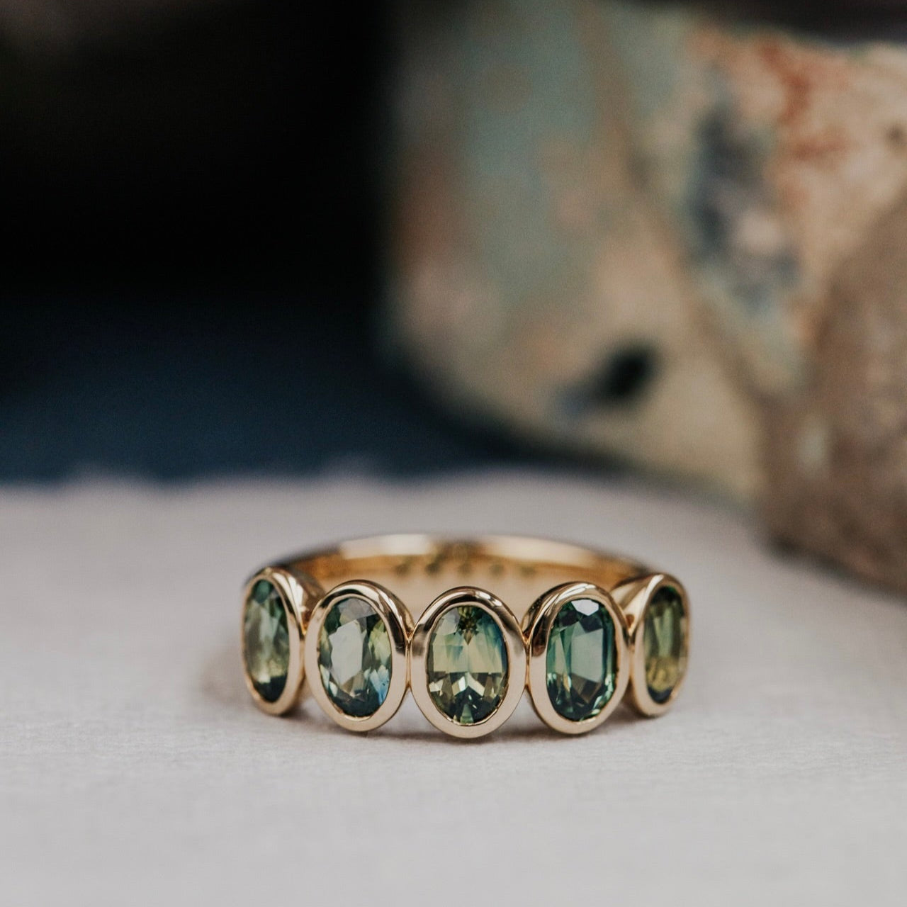 Gold ring with green Australian sapphire gemstones on a textured surface