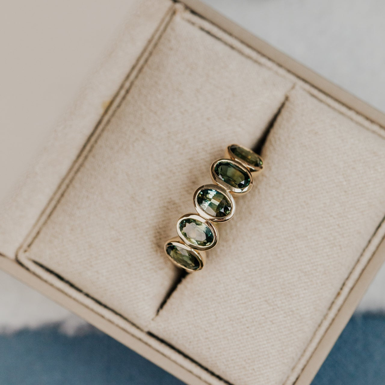 Gold ring with green Australian Sapphire gemstones on a beige jewelry box