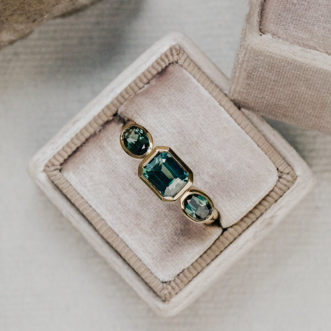 Gold ring with green Australian sapphire  gemstones on a beige velvet cushion