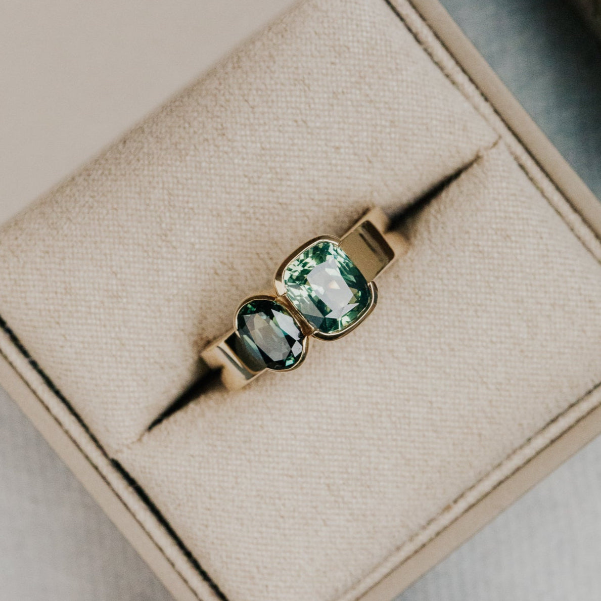 Gold ring with green and blue Australian sapphire  gemstones on a beige jewelry box