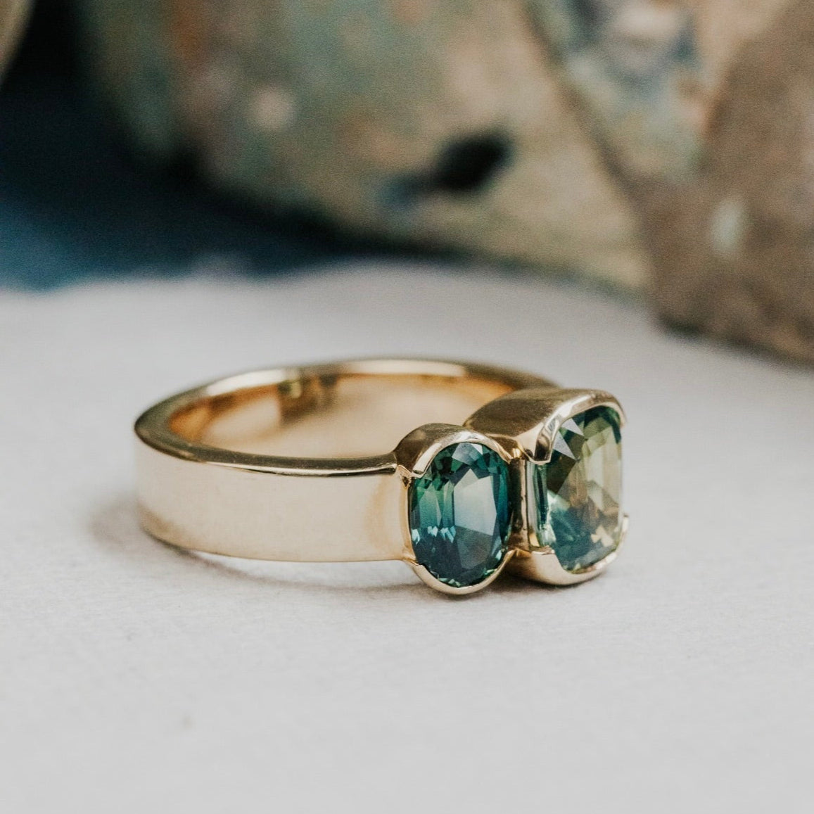 Gold ring with two green and blue Australian sapphire  gemstones on a neutral background