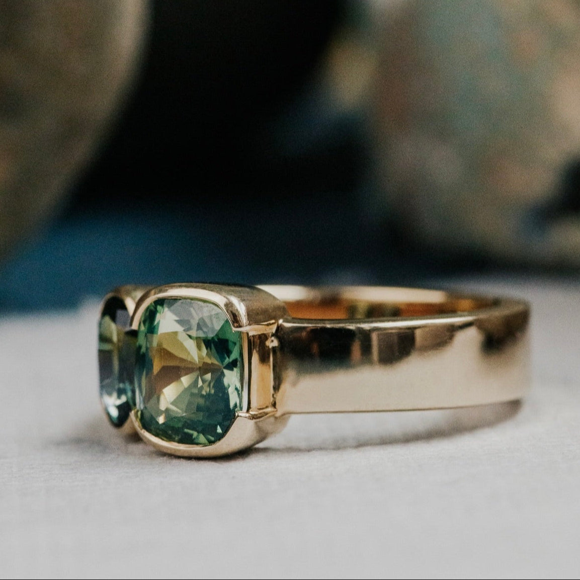 Gold ring with green and blue Australian sapphire gemstone on a neutral background
