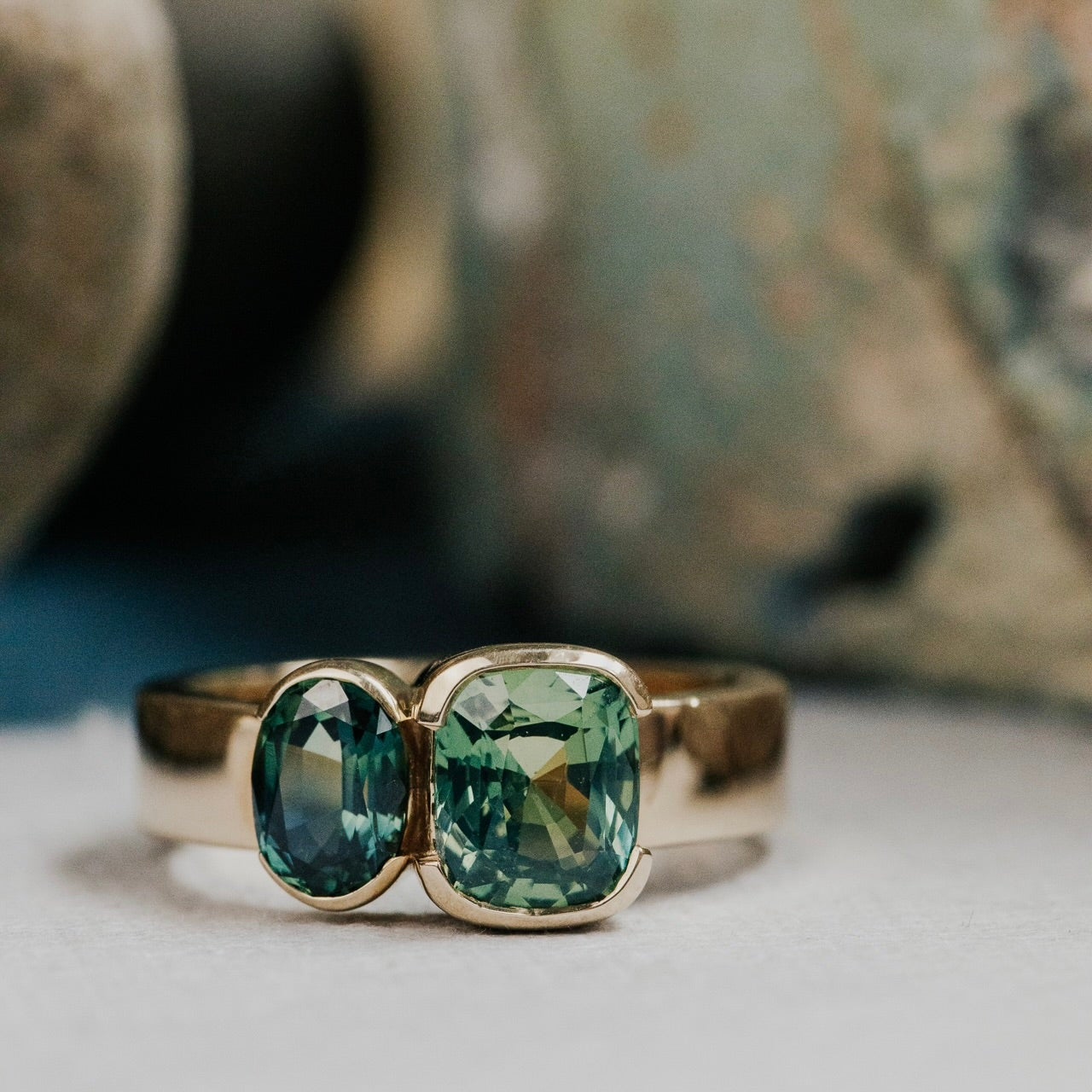 Gold ring with green and blue Australian sapphire gemstones on a neutral background