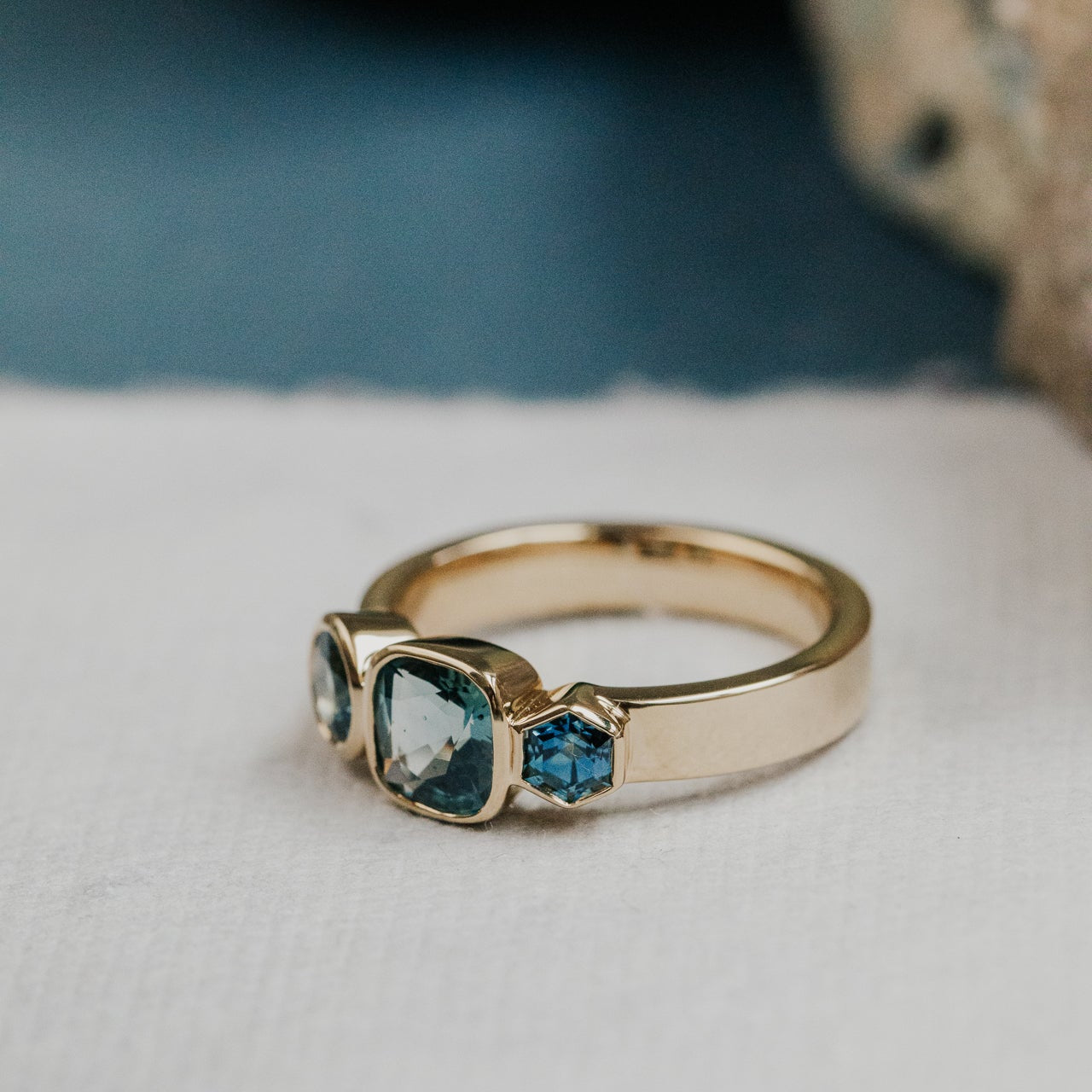 Gold ring with blue cushion blue Australian sapphire gemstones on a textured surface