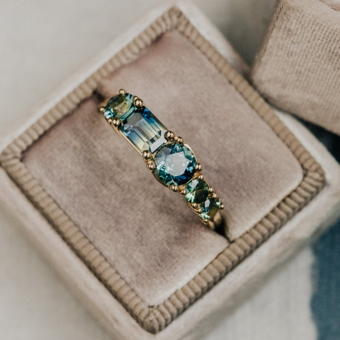 Gold ring with blue Australian sapphire gemstones on a beige cushion