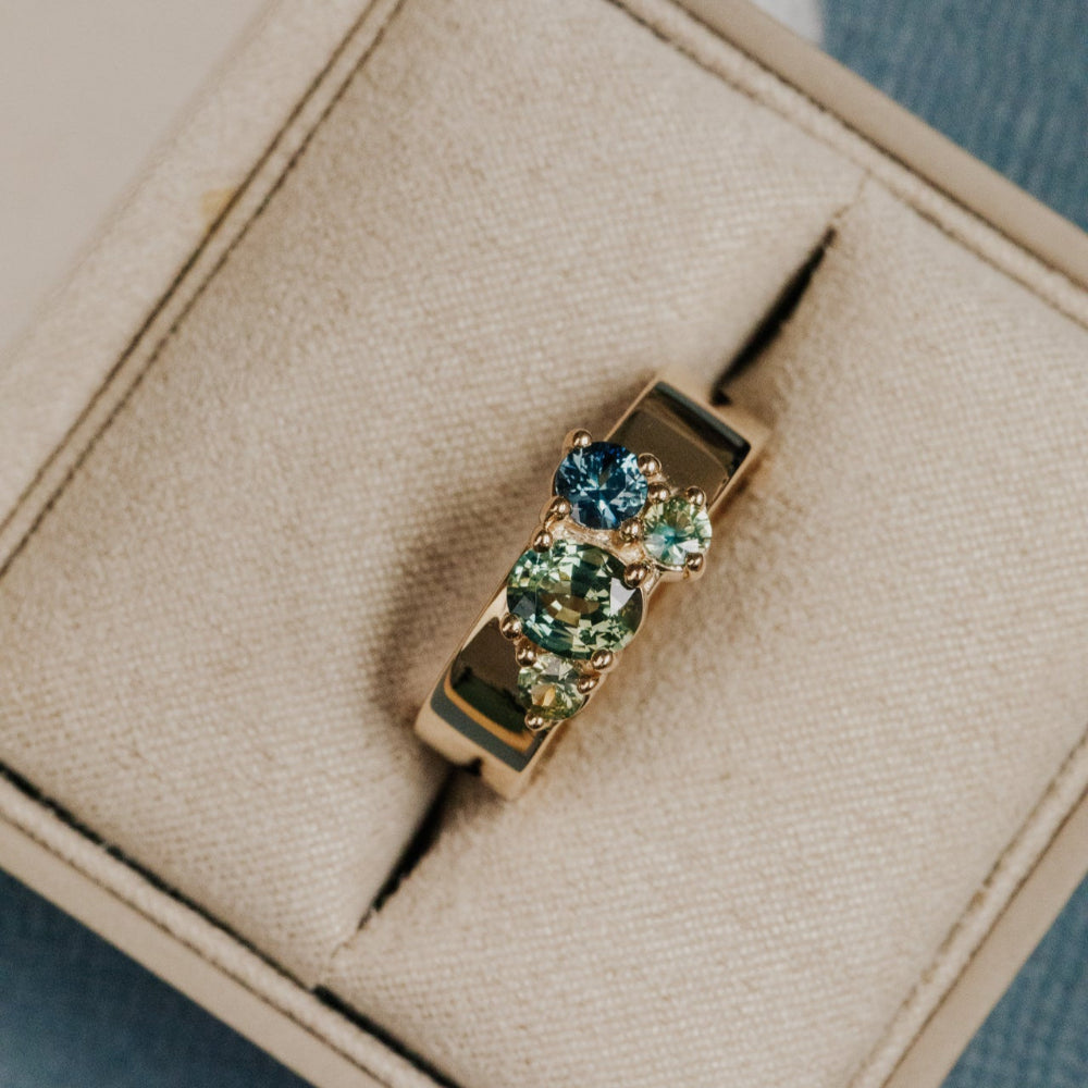 Gold ring with green Australian Sapphire gemstones on a beige cushion