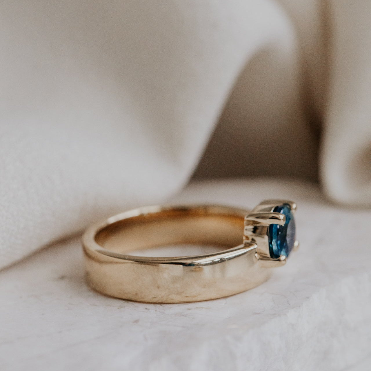 Gold Sezanne ring with a blue Montana sapphire on a soft beige background.