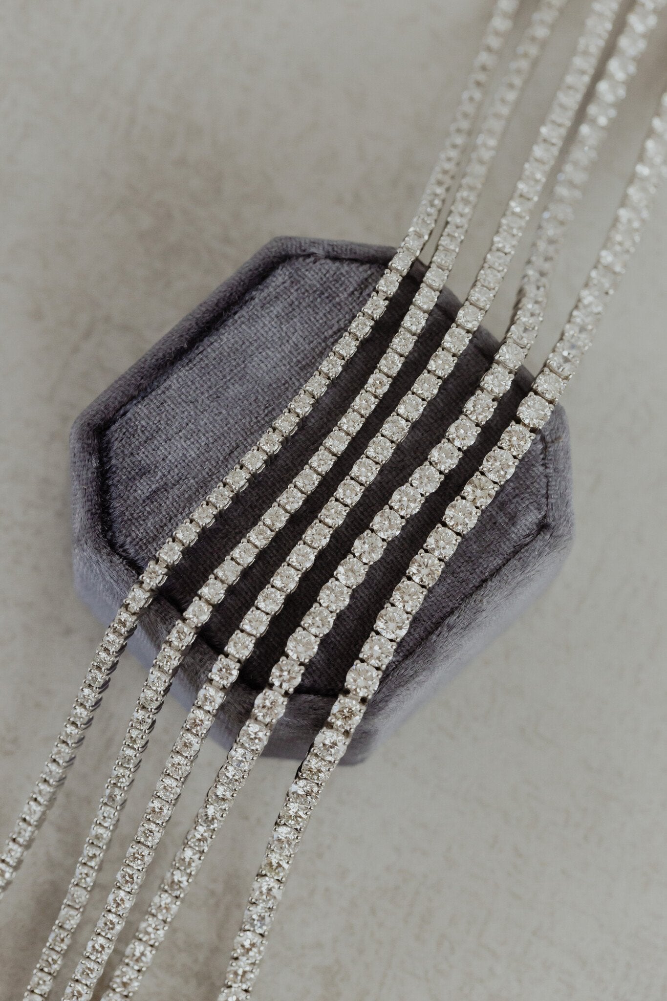 Five white gold signature diamond tennis bracelets in different sizes laid on top of a blue velvet box.