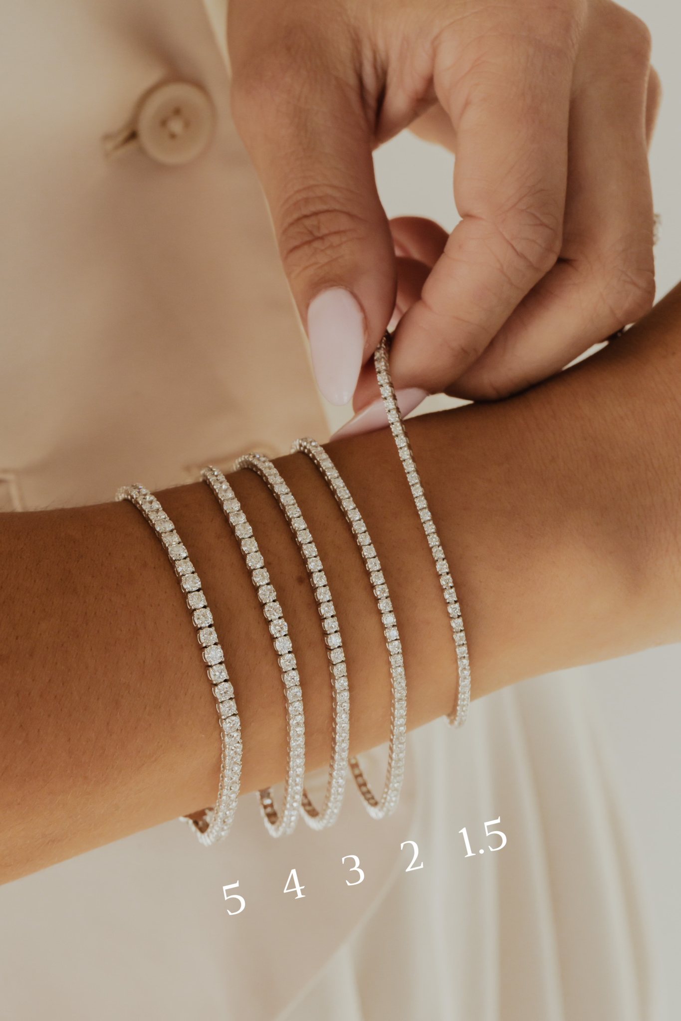 Close up of a person wearing multiple signature diamond tennis bracelets with size labels.