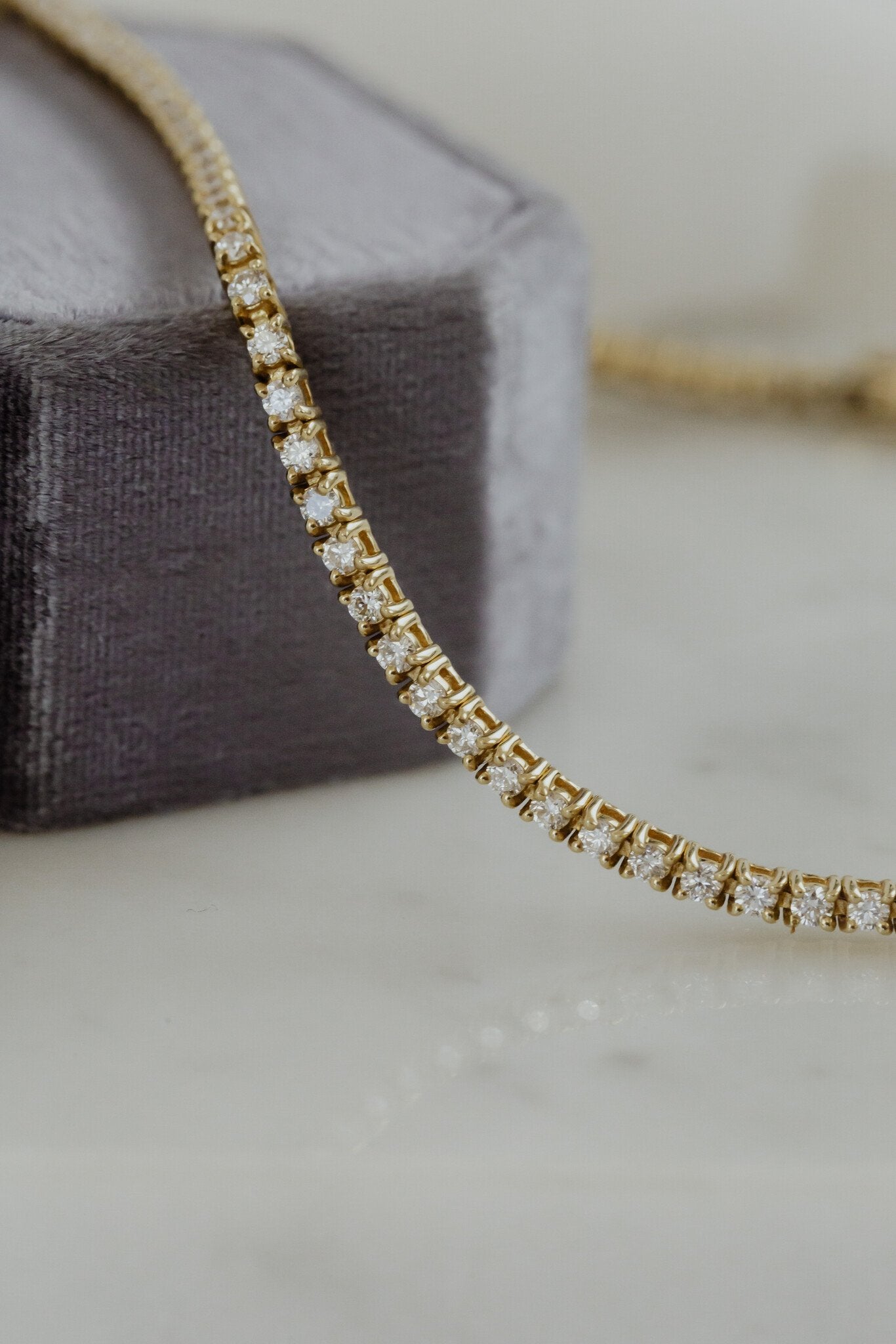 Side view of a gold signature diamond tennis bracelet on a neutral background.