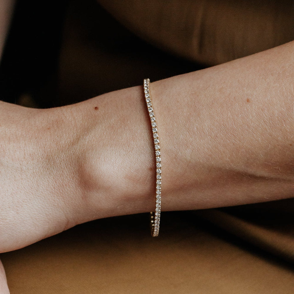Close-up of a person's wrist wearing a signature diamond tennis bracelet on a brown background.