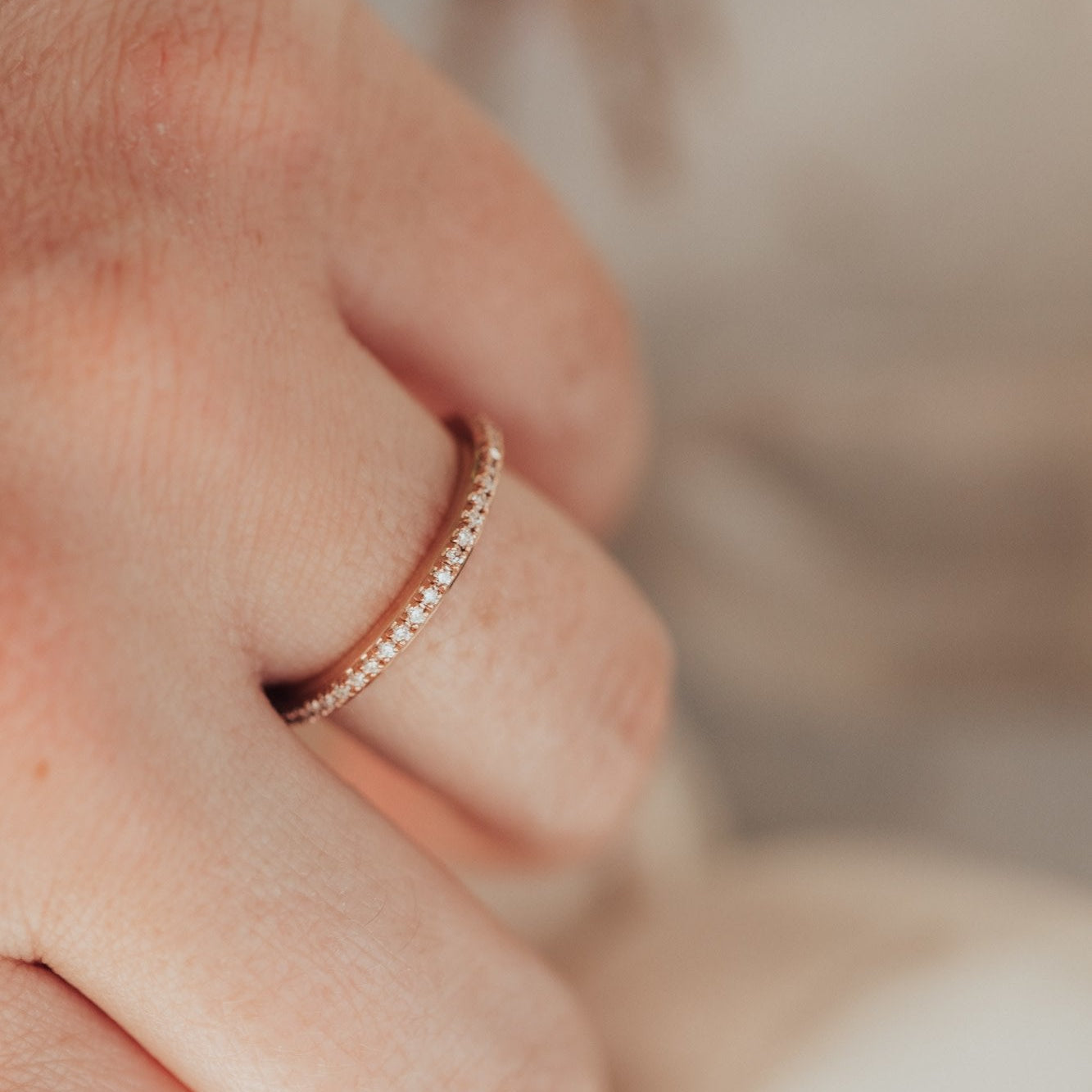 Close-up of a hand wearing the single row diamond wedding band in rose gold with a blurred background.