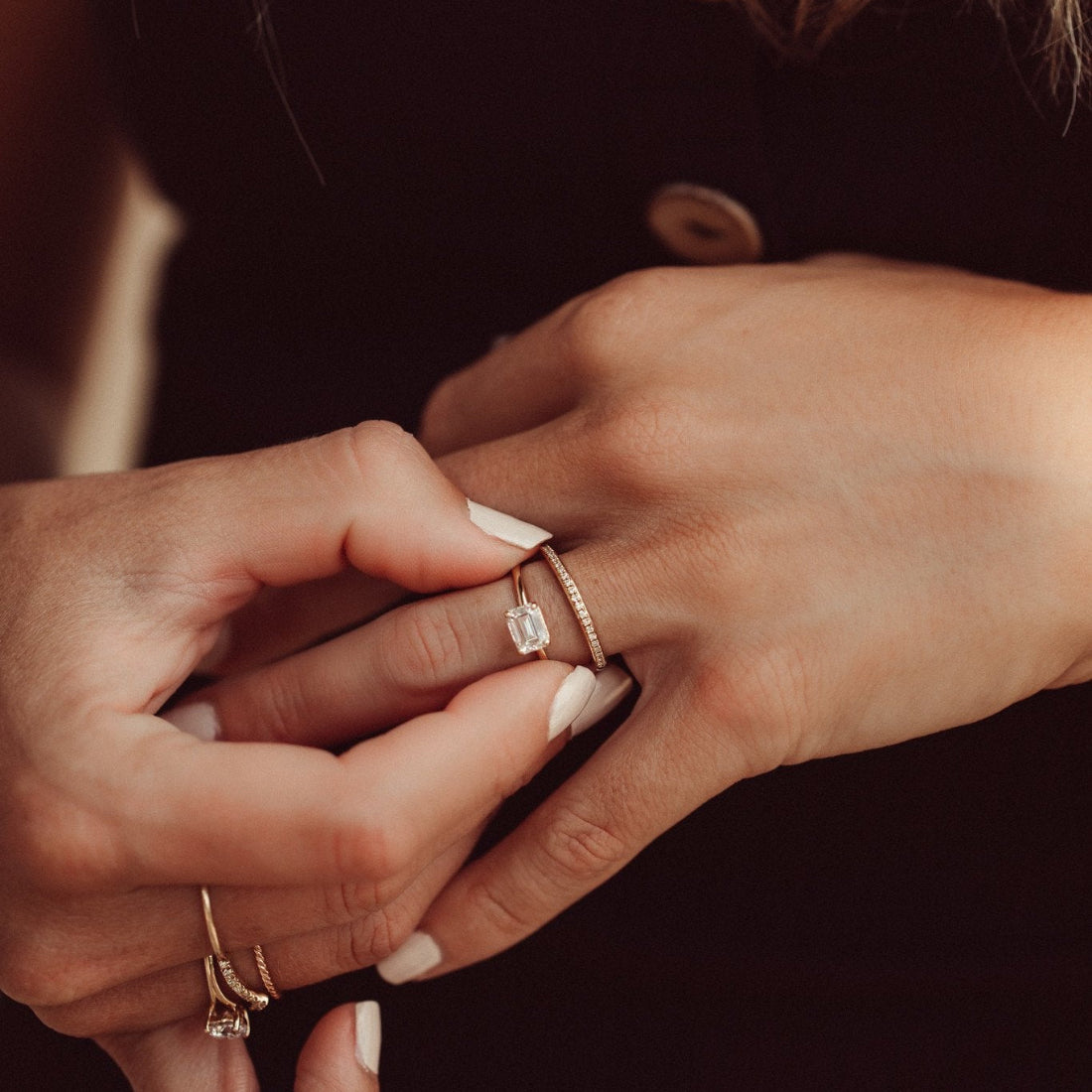 Close-up of hand wearing the Bennett emerald cut diamond engagement ring paired with the single row diamond wedding band on a dark background.