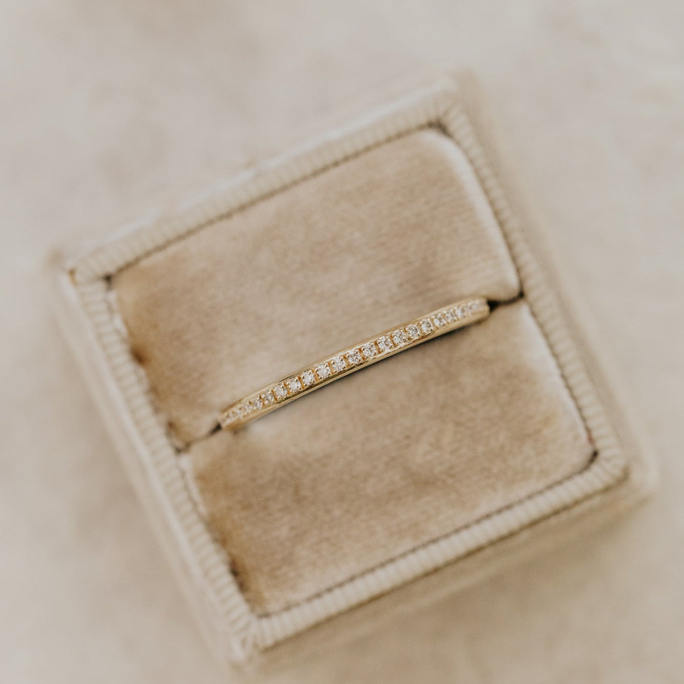 Yellow gold single row diamond wedding band in a beige jewelry box.