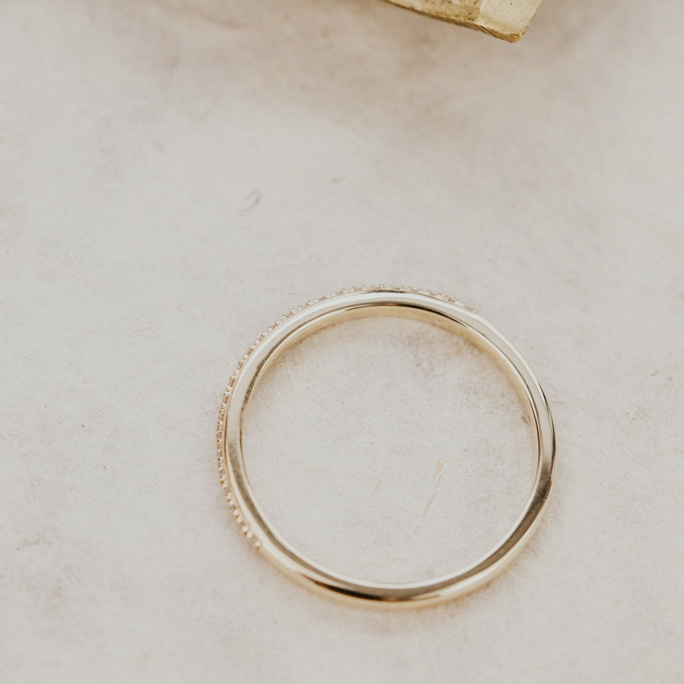 Gold single row diamond wedding band on a light beige surface.