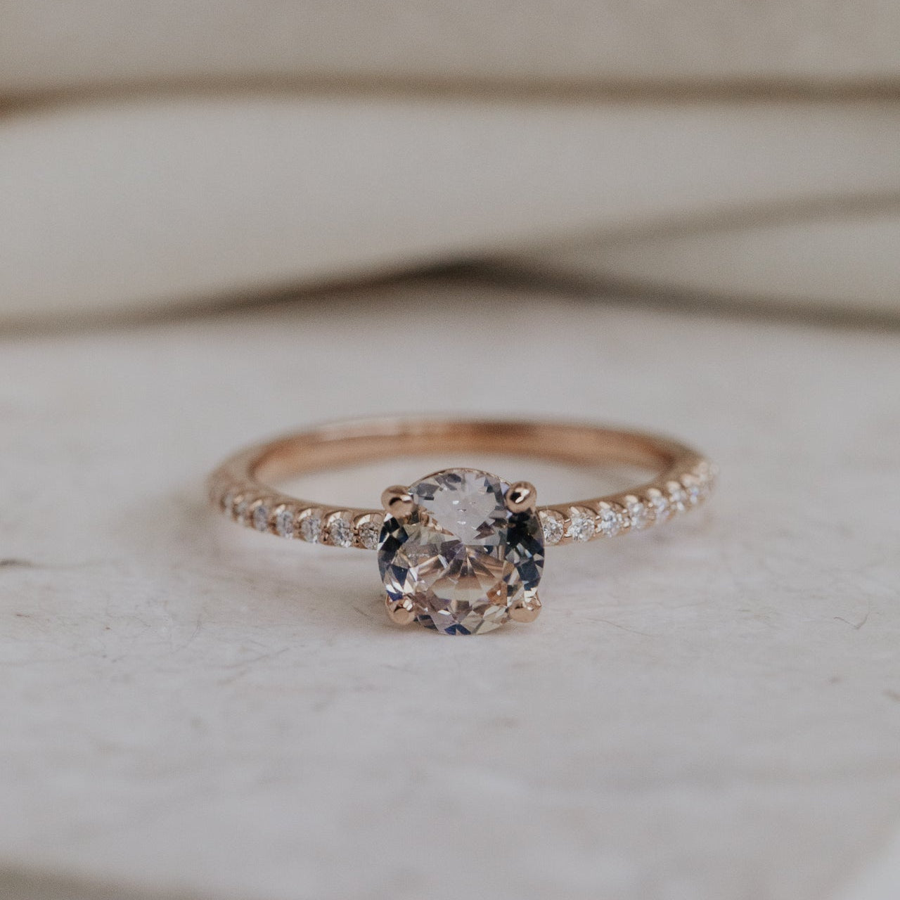 Rose gold ring with a light pink Sri Lanka Sapphire and a pave diamond band on a light wooden background