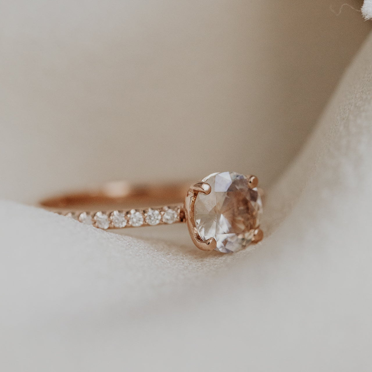 Rose gold ring with a light pink Sri Lanka Sapphire and a pave diamond band on a soft beige background