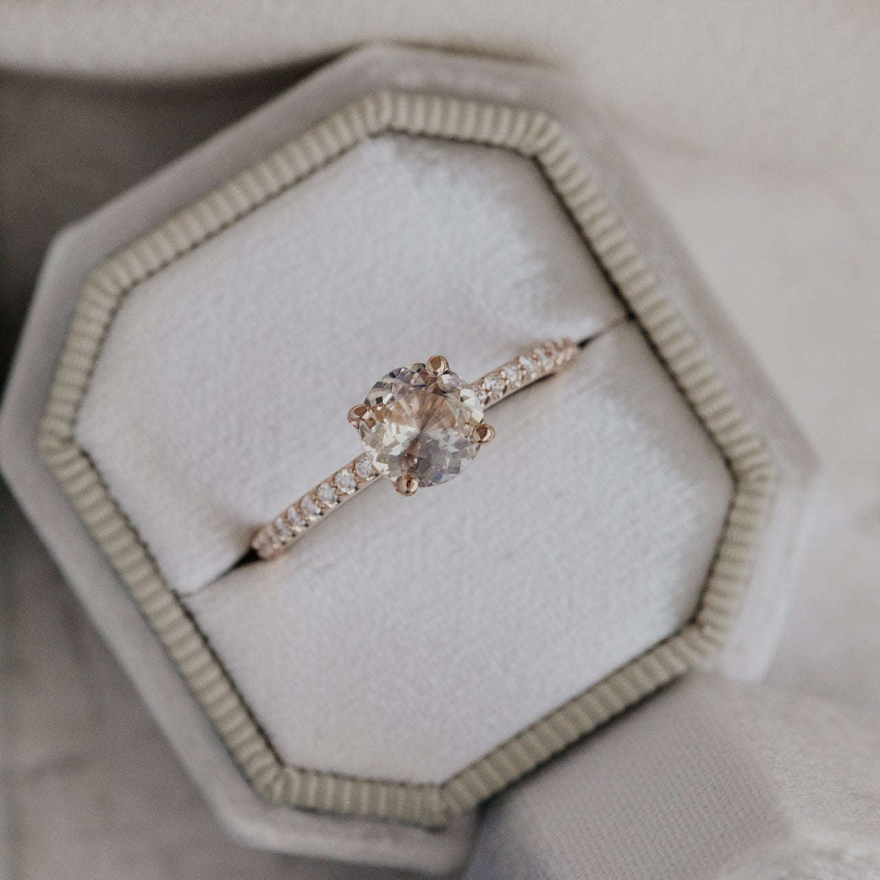 Rose gold ring with a light pink Sri Lanka Sapphire and a pave diamond band in a hexagonal box on a light background