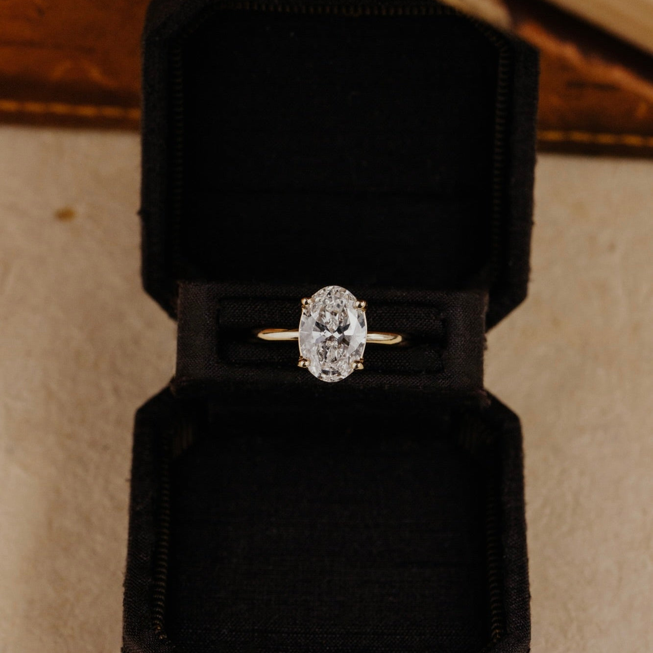 Oval diamond solitaire engagement ring in a black velvet box with a neutral background