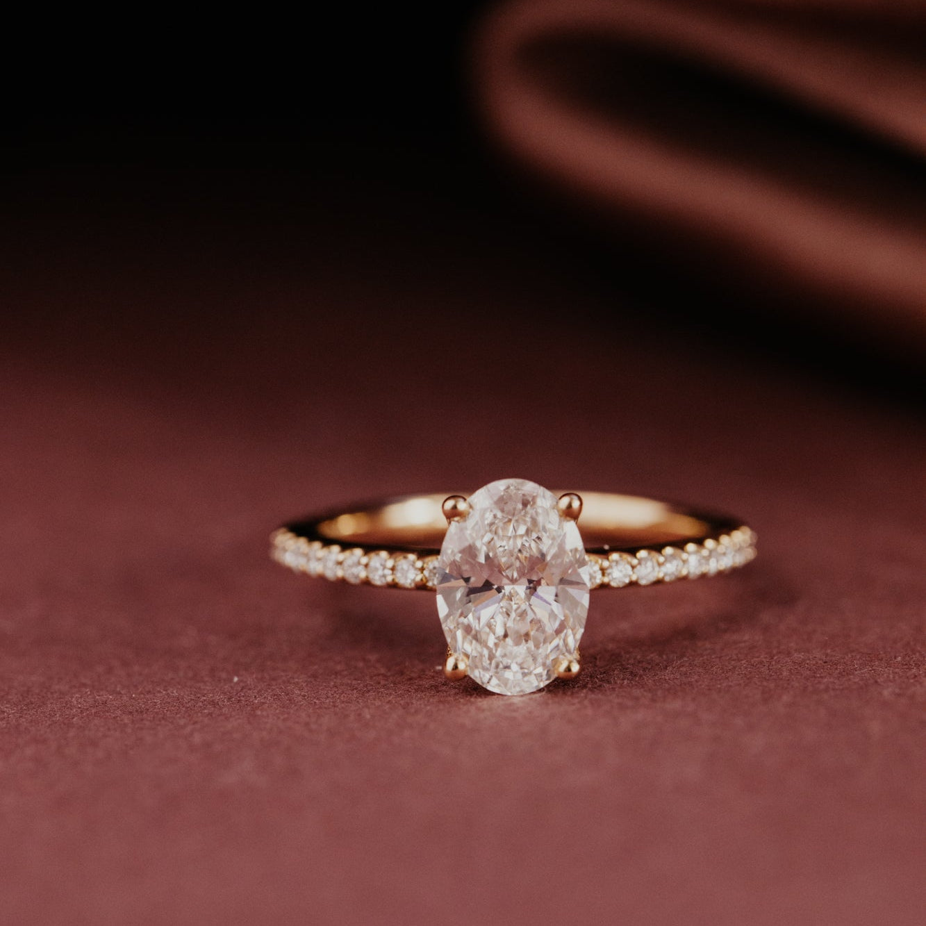 Oval shaped diamond engagement ring with a pave diamond band on a dark brown surface