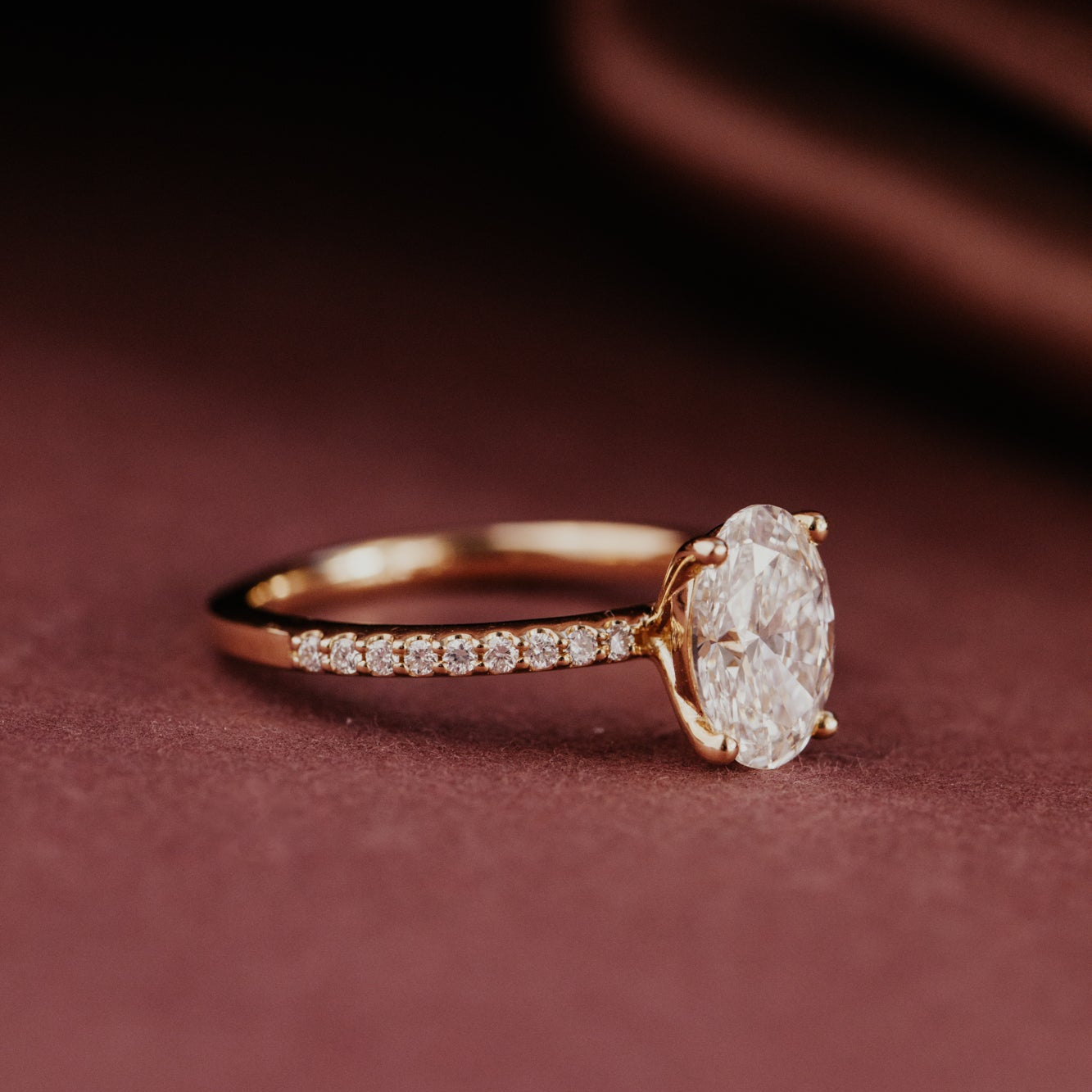Yellow gold ring with a large oval diamond and a pave diamond band on a red background