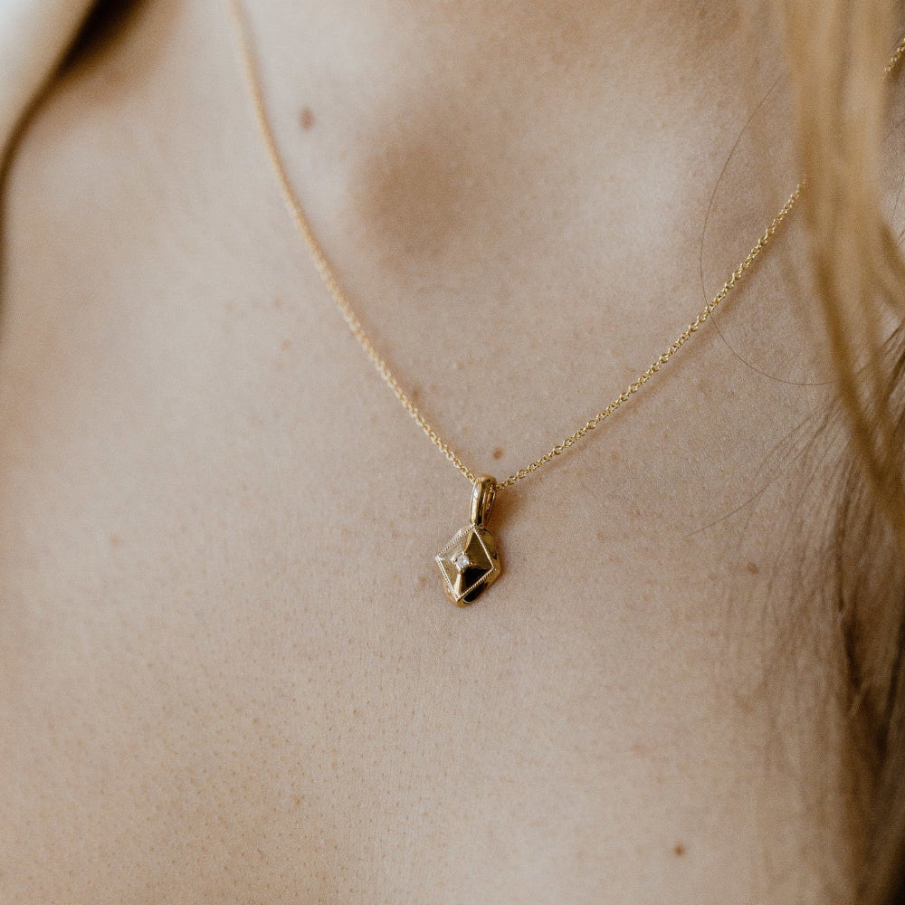 Gold necklace with a geometric charm on a person's neck