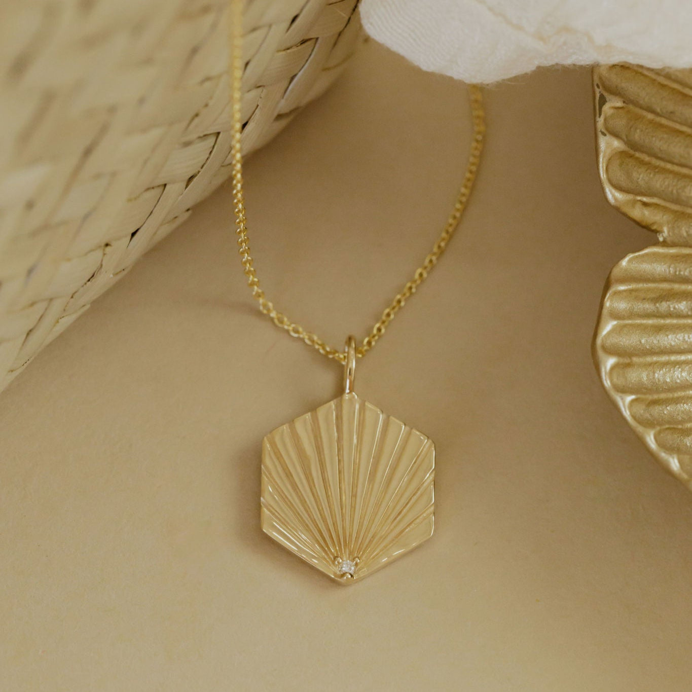 Gold necklace with a shell charm with a diamond accent stone on a beige background