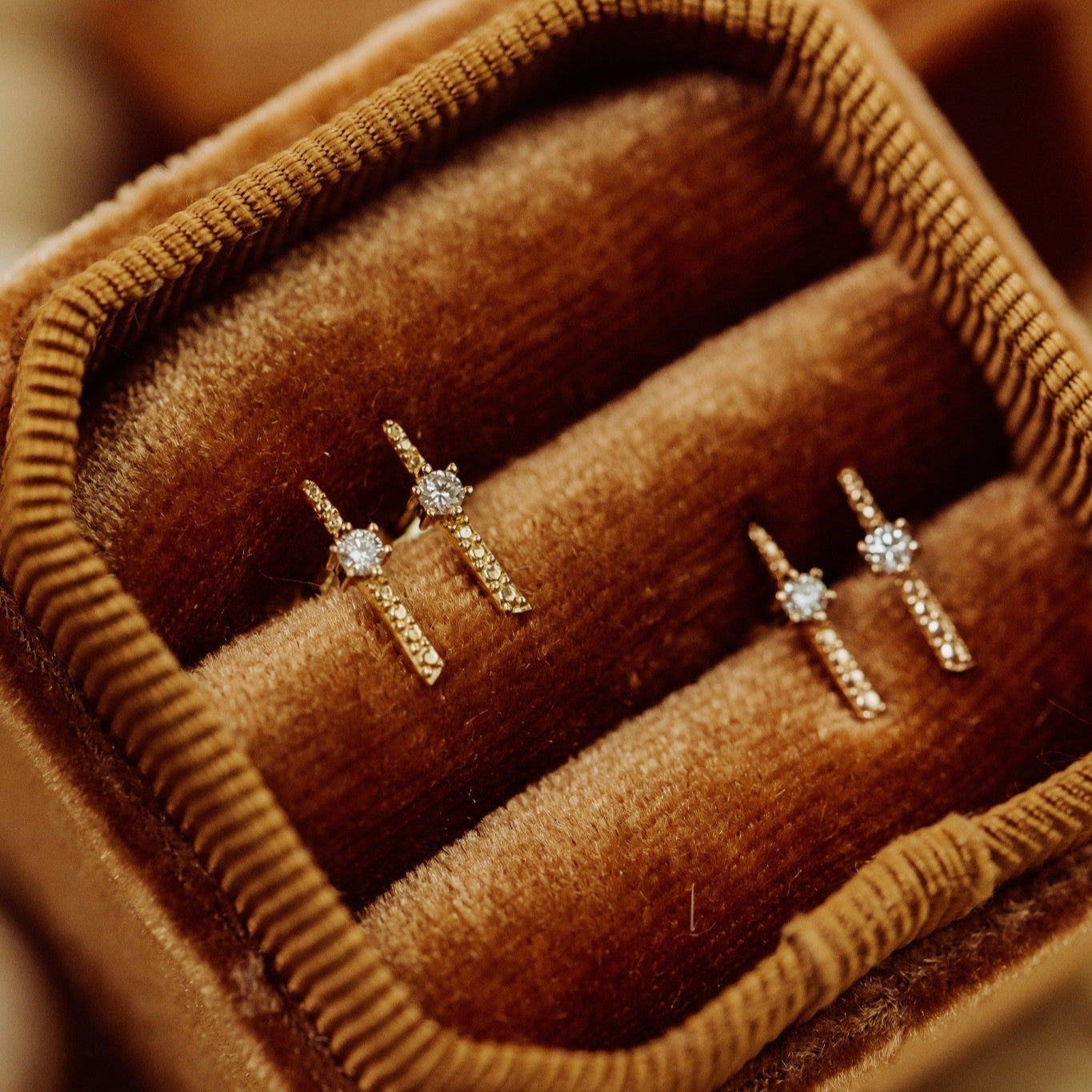 A pair of 14k gold diamond stud earrings with a beaded bar design, displayed in a brown velvet box.