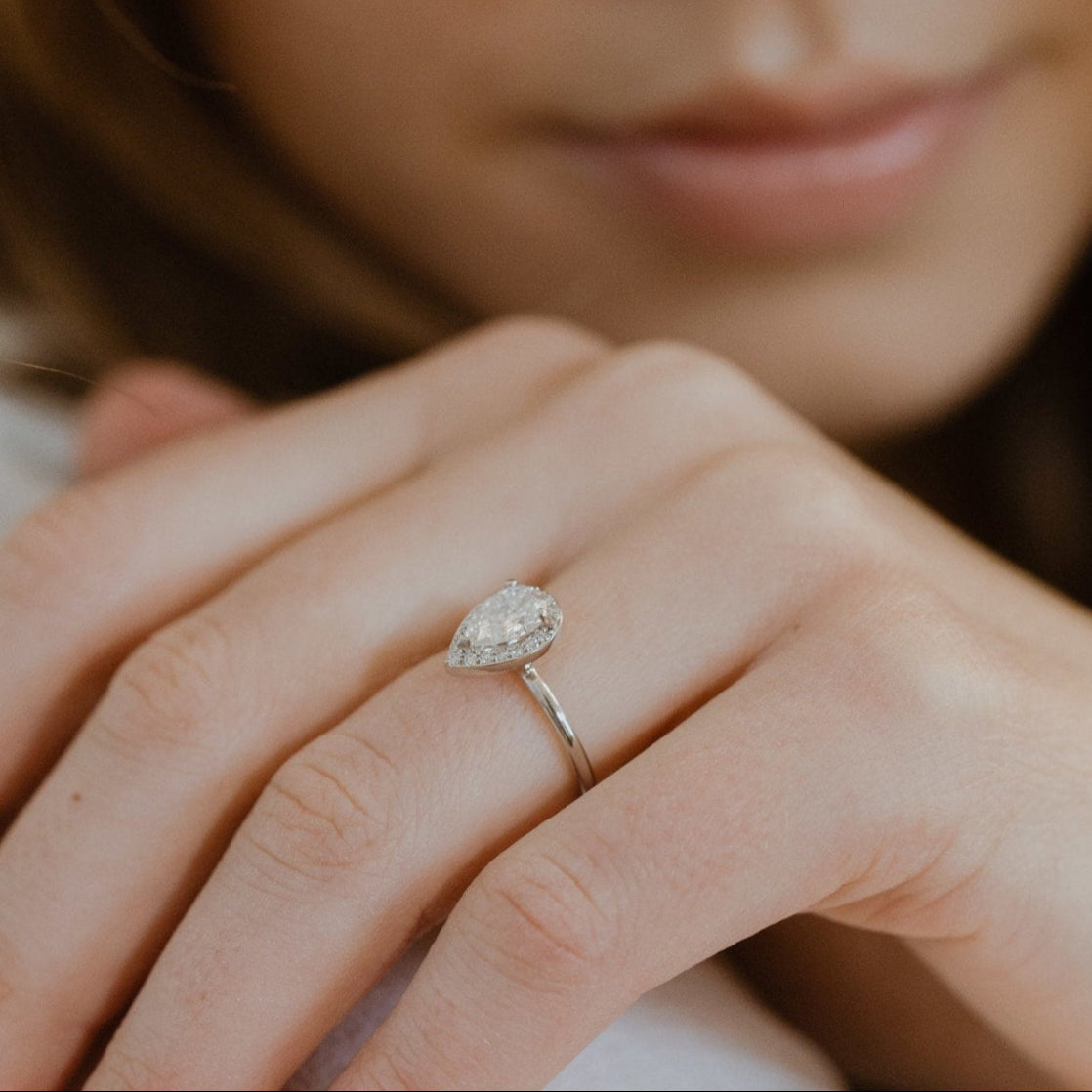 Close-up of a hand wearing a pear-shaped diamond ring with a blurred background