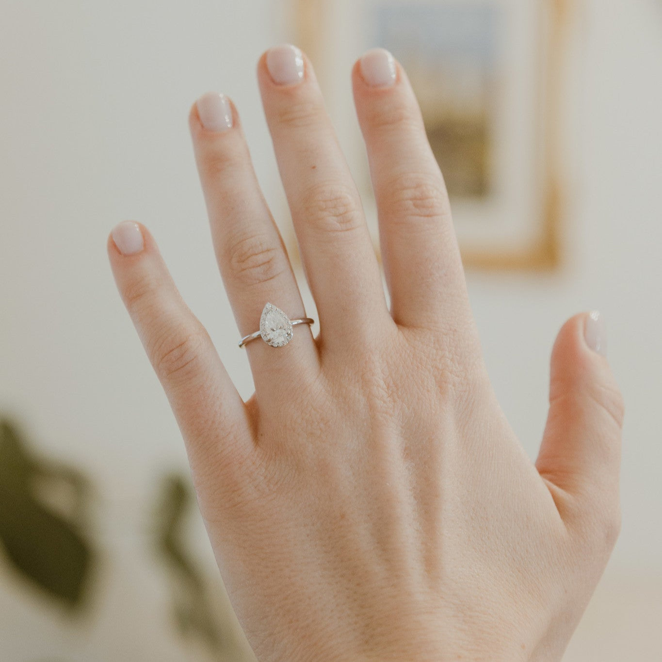 Hand wearing a pear-shaped diamond ring with a blurred indoor background