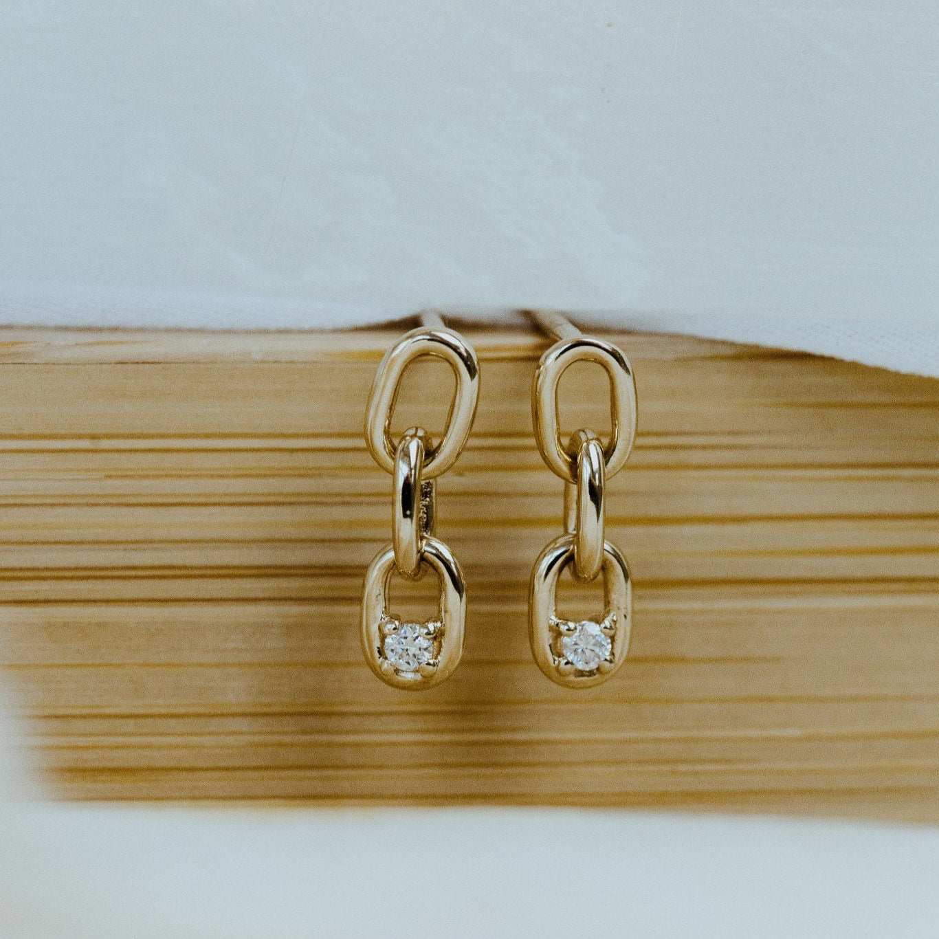 A pair of gold chain link earrings with a diamond set in one of the links, displayed on a white surface.