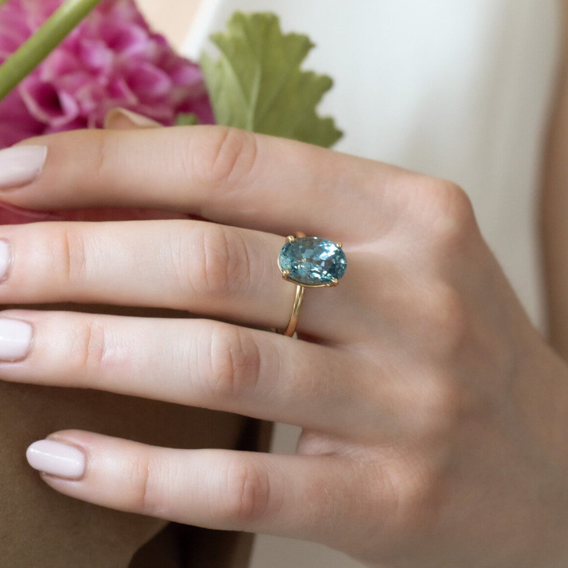 Hand wearing a gold ring with a blue gemstone, holding flowers.