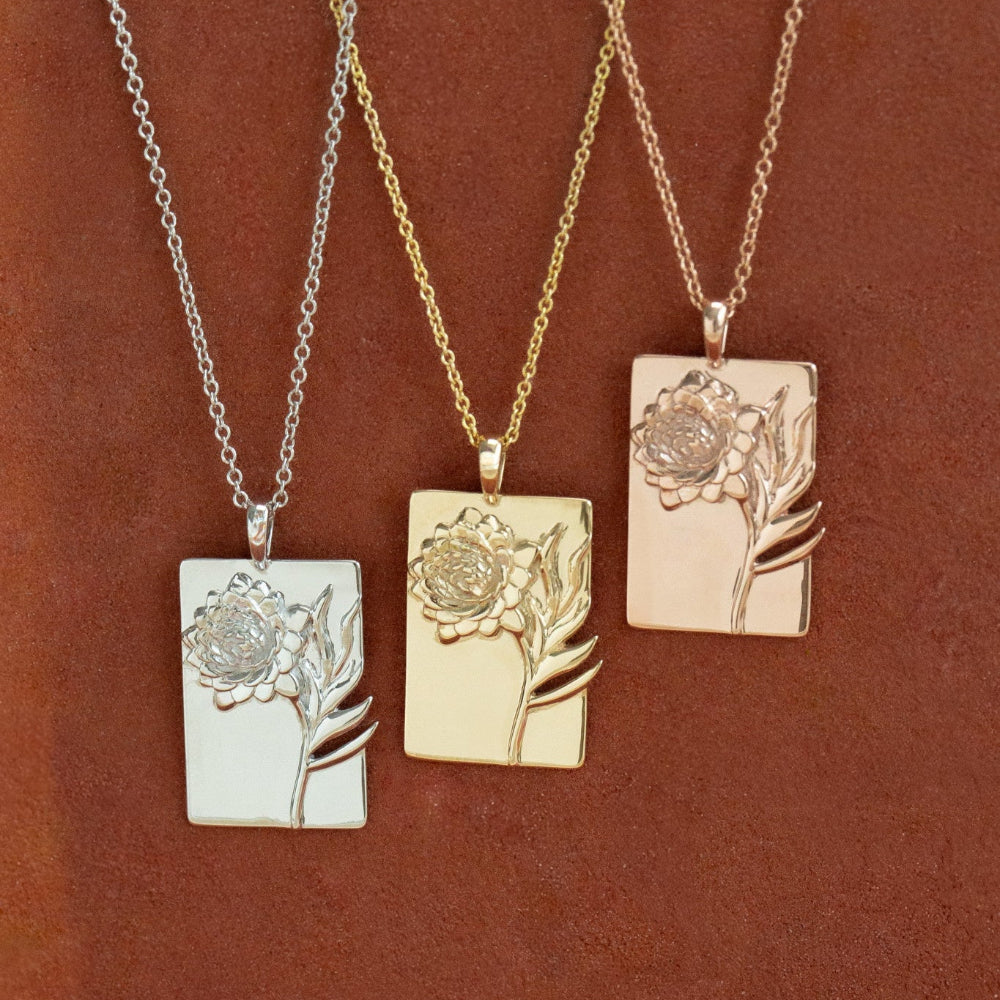 Three floral pendant necklaces in white gold, yellow gold, and rose gold on a brown background.