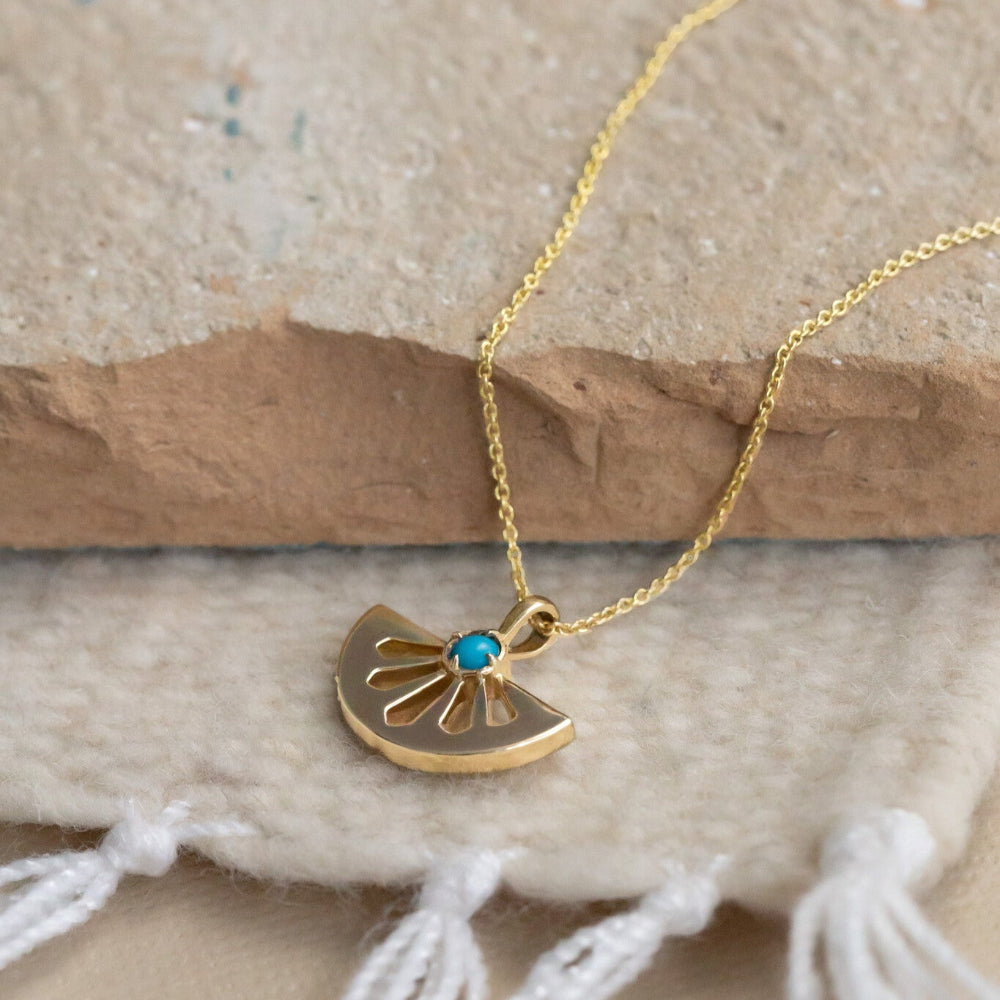 Gold necklace with a pendant featuring a teal gemstone on a textured surface.