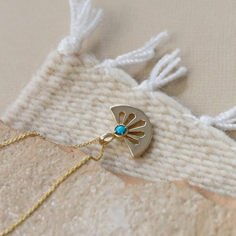 A 14k gold necklace with a cutout fan shape pendant and round turquoise stone set in a high polish bezel, displayed on an adjustable rolo chain.