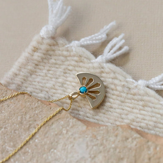A 14k gold necklace with a cutout fan shape pendant and round turquoise stone set in a high polish bezel, displayed on an adjustable rolo chain.